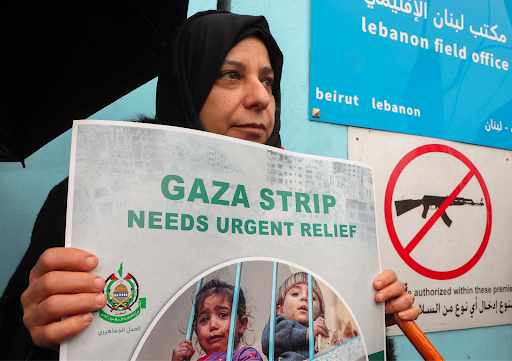 Woman holds “Gaza Strip Needs Urgent Relief” sign in front of the UNRWA Lebanon office
