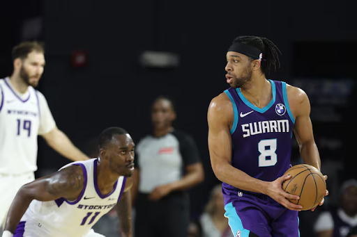 A man in a purple and blue basketball jersey holds a basketball while another man in a white and purple jersey plays defense during a Greensboro Swarm game.